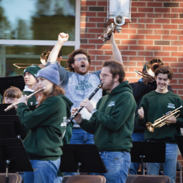 Titan Pep Band playing in front of State Farm Hall with one student raising a trumpet and cheering