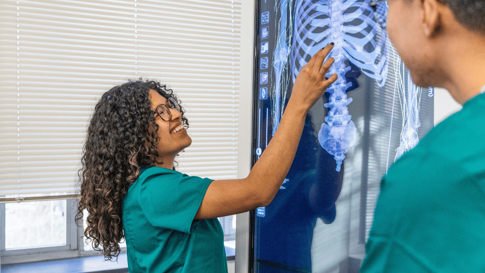 IWU nursing student in scrubs tapping a large monitor with a skeleton