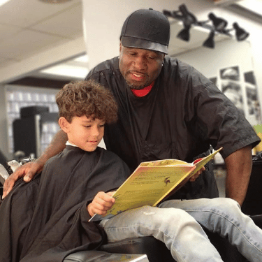 Child reads book with barber during haircut